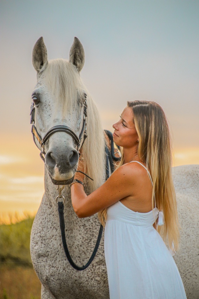 Alice Bonnissel aux côtés d'un cheval blanc au coucher du soleil